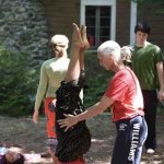 KJ, a white haired white woman assisting a dancer in an inversion